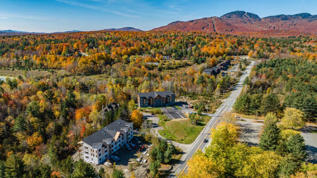 Vue aérienne des condos et habitations au pied du Mont-Orford, entourés de forêts colorées.